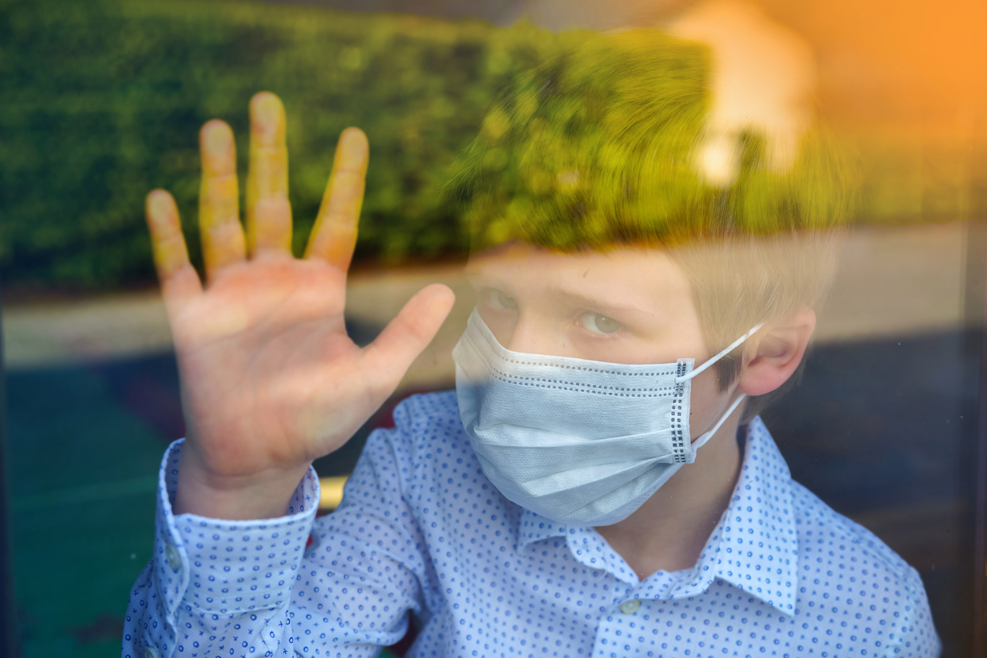 Junge mit Maske hinter Glas, symbolisiert Tabuthemen wie Bestattungen
