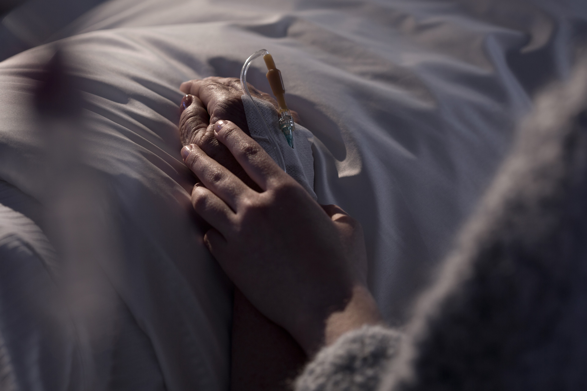 Hand eines Patienten in Palliativpflege, gehalten von einer nahestehenden Person – symbolisch für Sterbebegleitung.